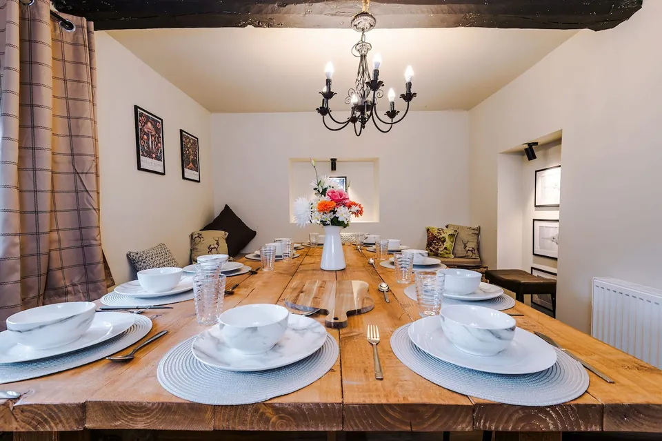 A long wooden dining table laid with white bowls, plates and glasses, with flowers and a chandelier above.