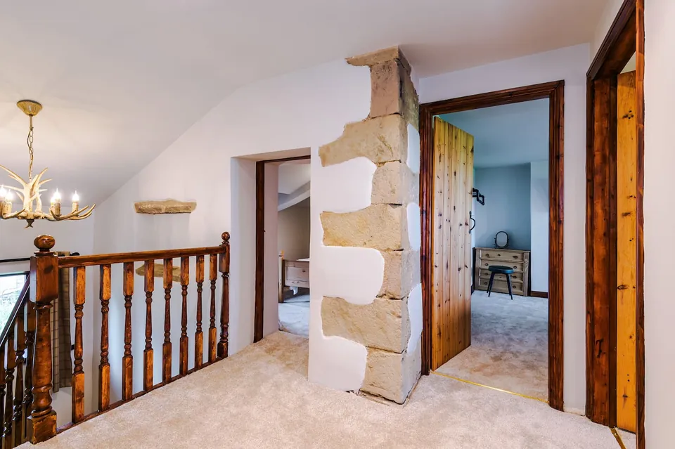 An upstairs landing with beige carpet, a wooden stair rail and a stone pier, opening onto rooms including one with a bed.