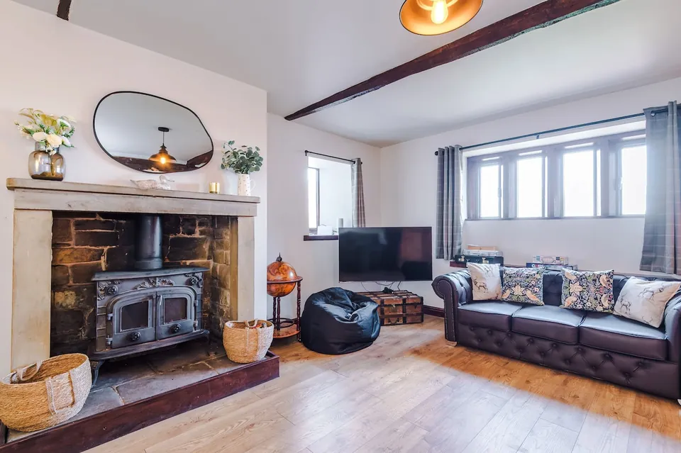 A living room with a black stove set in a fireplace, a television on the wall, and a dark leather sofa.